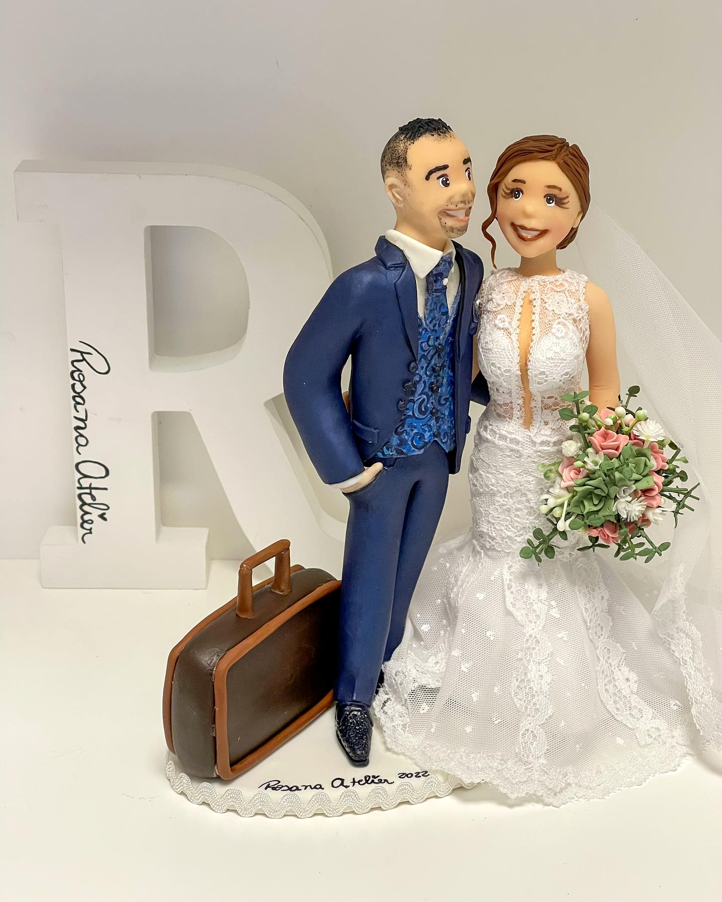 Retrato escultórico de um casal com mala, buquê e base assinada Rosana Atelier
